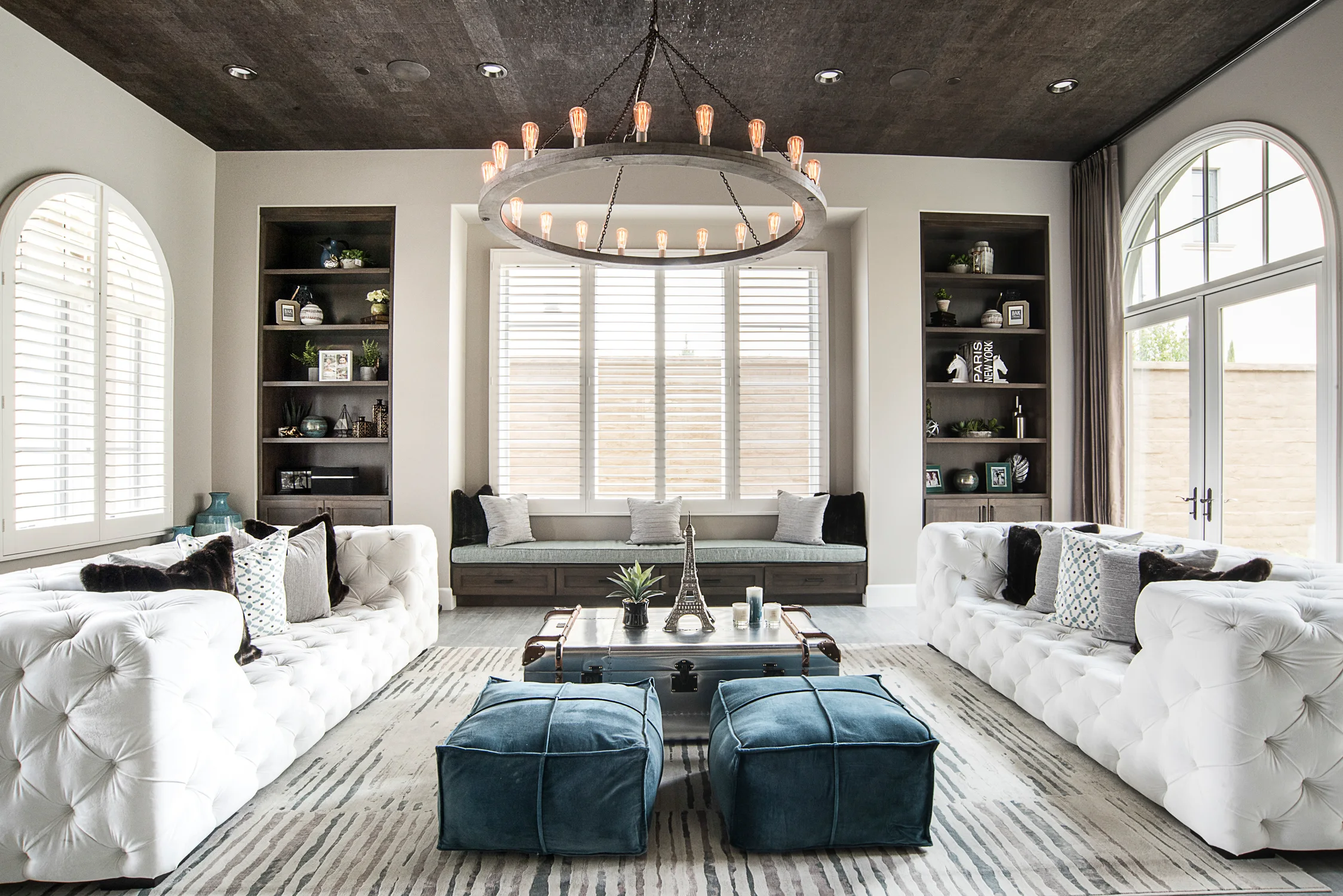 Living room with white tufted sofas, blue ottomans, and a circular chandelier