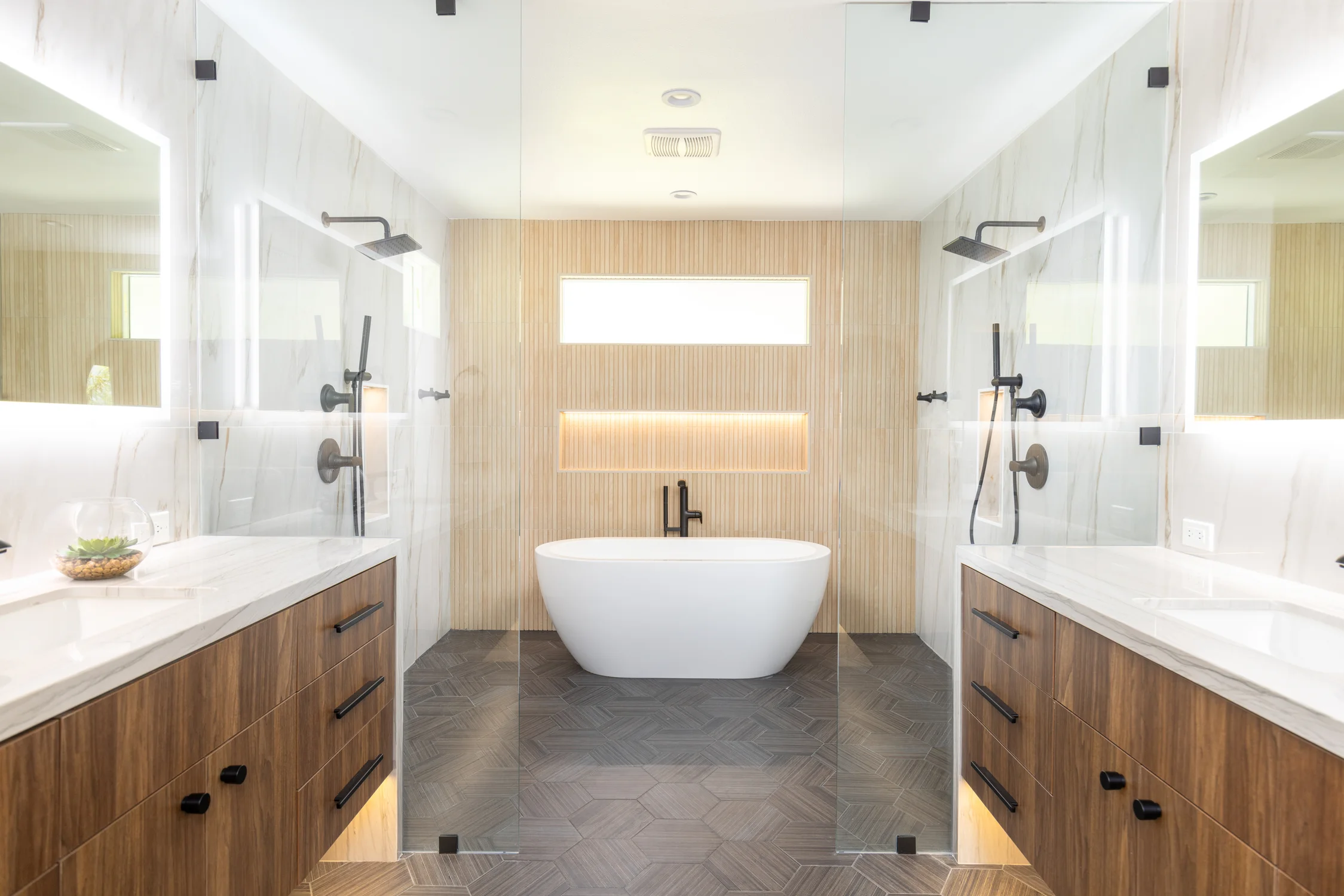 Bathroom with a freestanding tub between glass showers and wood vanities
